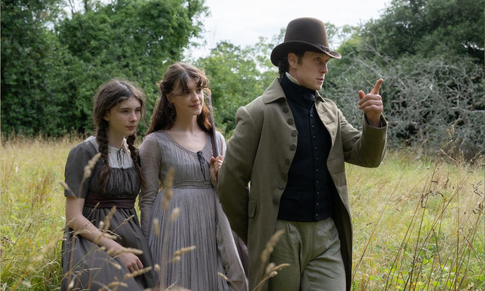 Bodhi Rae Breathnach stars as Margaret Dashwood, Daisy Edgar-Jones as Elinor Dashwood and George MacKay as Edward Ferrars in SENSE and SENSIBILITY film. Standing in a countryside field together.